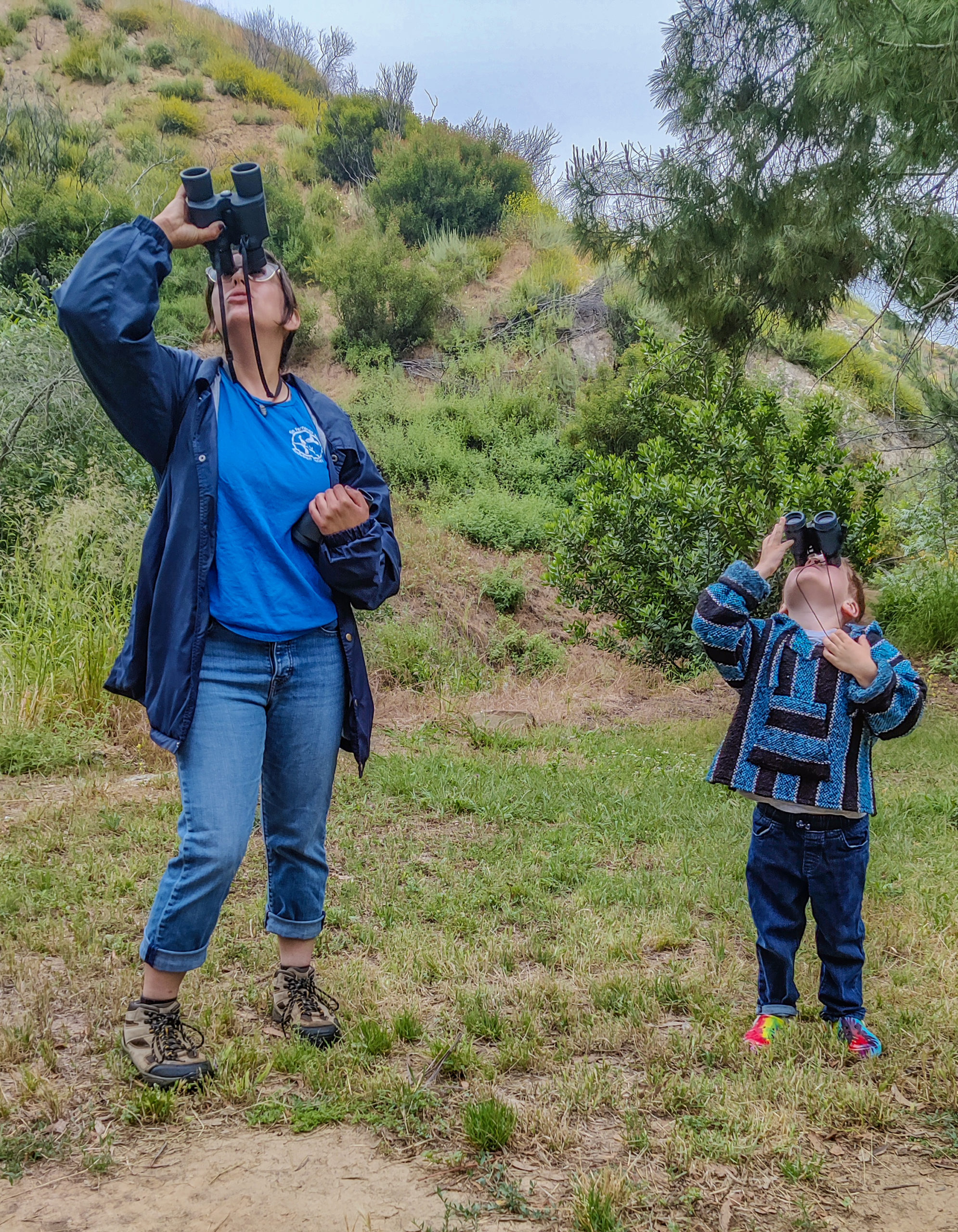 A person and child looking through binoculars Description automatically generated